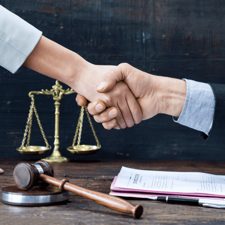 Stock image of 2 hands shaking in front of a justice scale and gavel