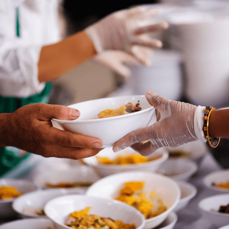 Photo of a gloved hand passing a bowl of food to someone