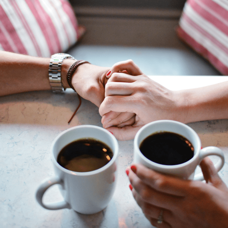 Two people holding hands with coffee cups set in front of their hands.