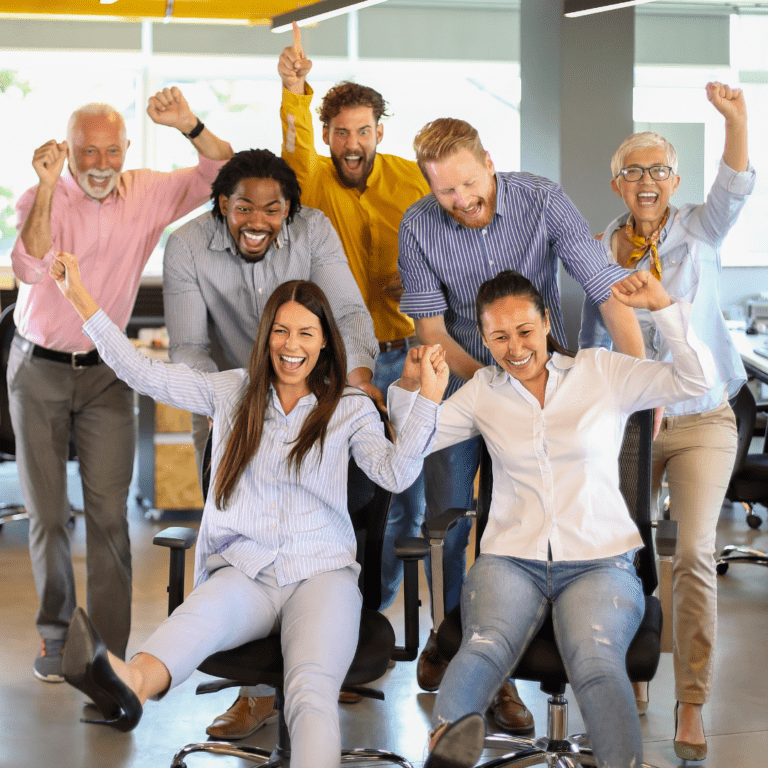 Group of seven people in an office type setting all with happy expressions on their faces and their hands up in the air like they're cheering